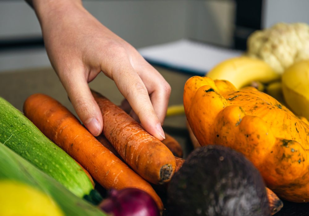 Close-up, a woman's hand takes a carrot among the vegetables on the kitchen table for cooking.