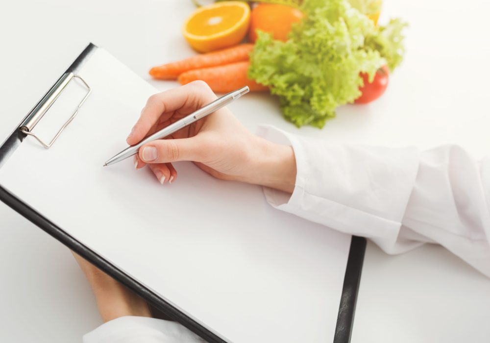 Nutritionist doctor writing diet plan on table. Unrecognizable dietitian making healthy eating menu, copy space for text. Right nutrition and slimming concept