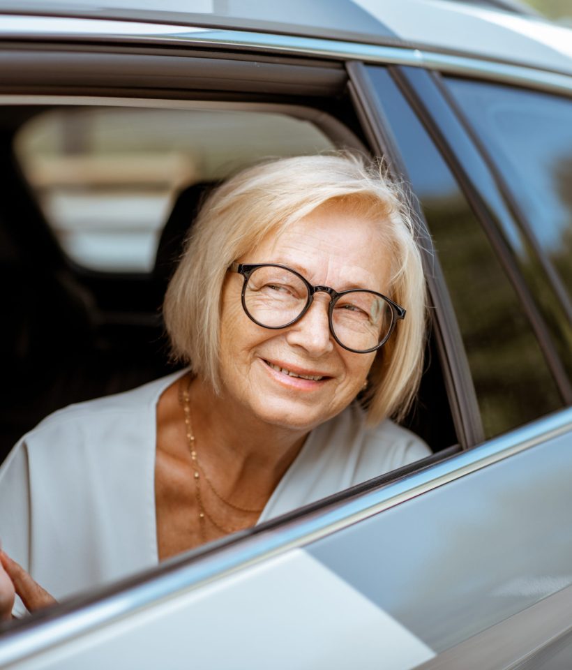 Portrait of a happy senior business woman looking out the car window, traveling on the back seat of a taxi